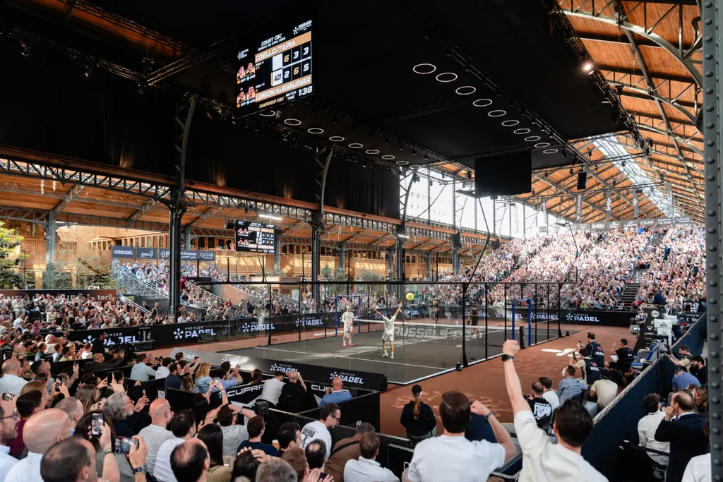 Players on the Central Court under the steel roof of the Gare Maritime, with the crowd around the glass court